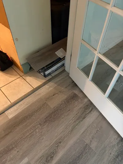 New grey vinyl plank flooring being installed next to existing tile near a glass-paned door.