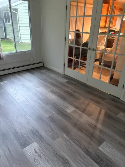 Empty sunroom with grey vinyl plank flooring, a sliding glass door, and French doors to the kitchen.