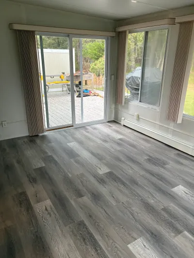 Living room with new grey plank flooring, a sliding glass door, and a window overlooking a wood deck.