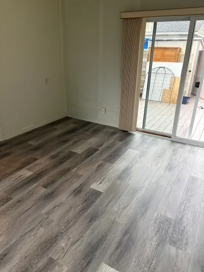 Empty room with new grey wood-look vinyl plank flooring and a sliding glass door to the deck.