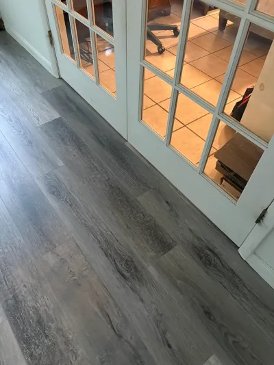 Grey wood-look vinyl plank flooring in a hallway leading to white French doors with glass panes.