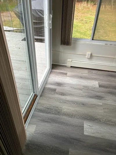 Gray plank flooring meets a sliding glass door with a deck and lawn visible outside.