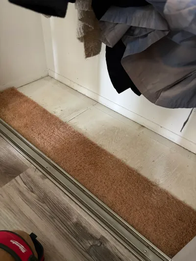 Closet floor mid-renovation showing old carpet remnant next to new plank flooring in the hallway.