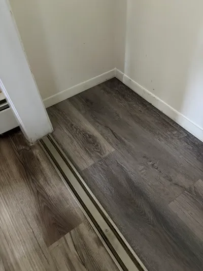 Close-up of dark wood-look vinyl plank flooring meeting at a metal threshold strip near a doorway.