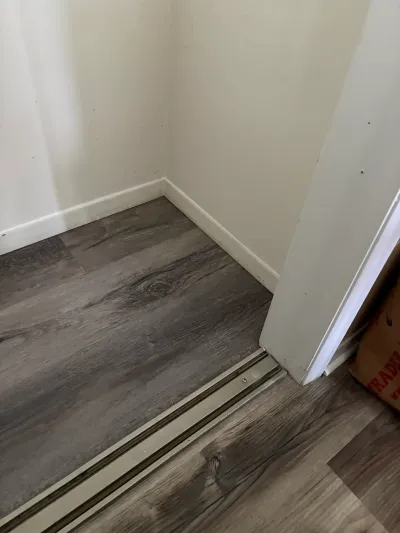 Corner of a closet with dark wood-look vinyl plank flooring and white baseboard trim.