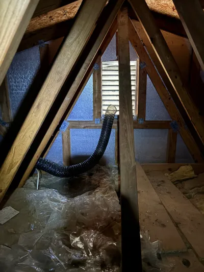 Unfinished attic with exposed rafters, a gable vent, and a flexible duct running across insulation.