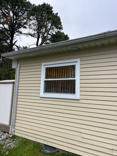 Side exterior wall of a house with cream vinyl siding, a white-trimmed window, and gutter downspout.