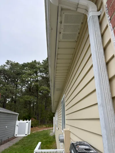 Side view of a house showing cream vinyl siding, a corner gutter downspout, and a soffit vent under the eave.