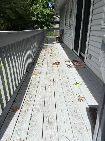 A weathered wood deck with peeling white paint runs along the side of a house with vinyl siding.