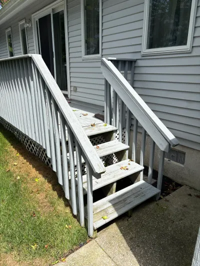 Weathered wood deck stairs with peeling white paint leading to a sliding door on a vinyl-sided house.