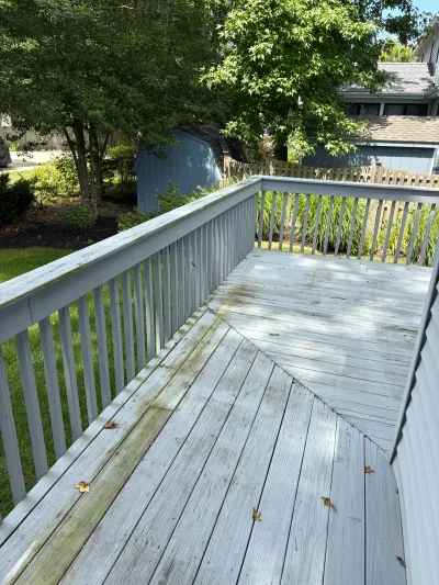 A weathered wood deck with peeling white railing and mildew stains, overlooking a shaded backyard.