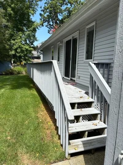 Weathered wood deck and stairs along the side of a house with gray vinyl siding.