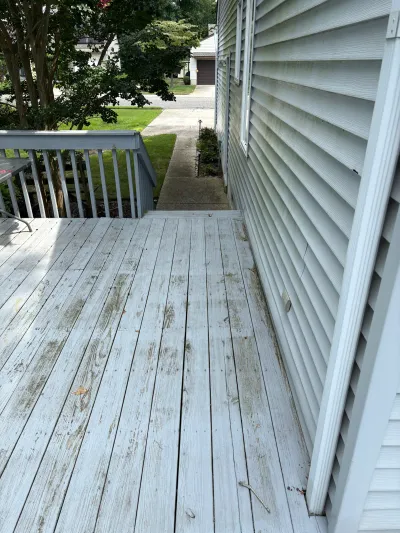 Weathered wood deck with graying boards next to a house, steps leading to a concrete walkway.