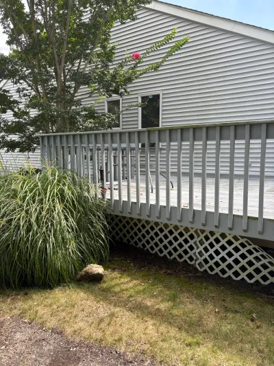 Weathered wood deck with damaged lattice skirting attached to a house with grey vinyl siding.