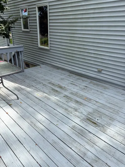 Weathered, stained wood deck boards beside a house with vinyl siding, before renovation.