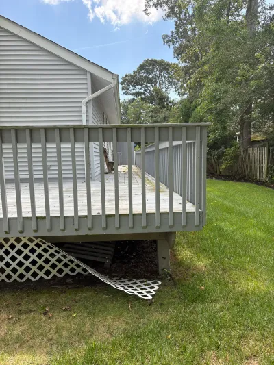 Weathered wood deck with damaged, hanging lattice skirting on the side of a house.