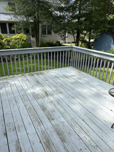 A weathered wood deck with peeling white railing overlooks a backyard with trees and a shed.