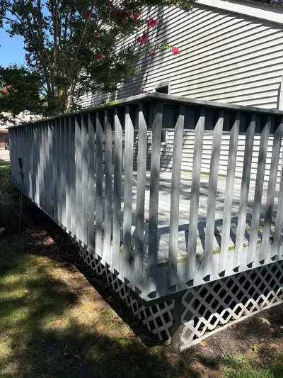 Weathered white wood deck with picket railing and lattice skirting beside a vinyl-sided house.