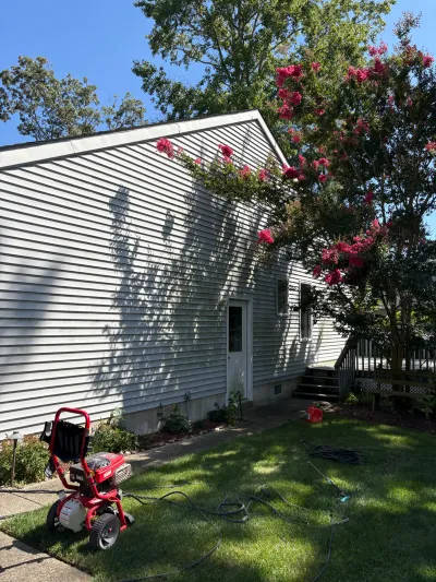 Side of a white vinyl-sided house with a wood deck, blooming pink crepe myrtle, and a lawn aerator on the grass.