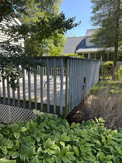 Weathered wood deck with grey railing and lattice skirting, surrounded by hostas and trees.