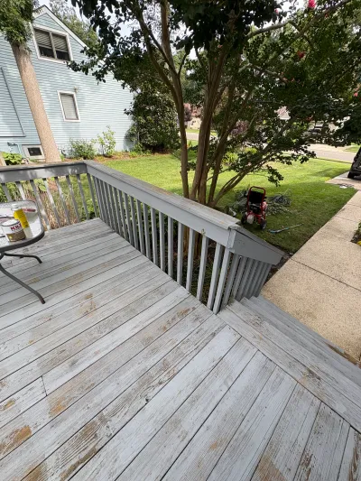 Weathered wood deck with peeling paint and railing, prepped for repainting, next to a yard and house.