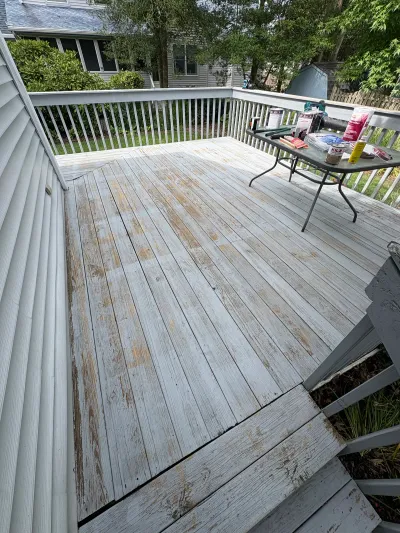 A weathered deck with peeling paint mid-refinishing, with primer and paint supplies staged on a table.