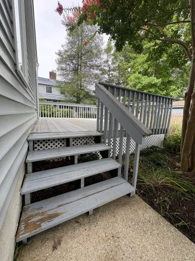 Weathered wooden deck stairs with peeling paint lead up to a backyard deck surrounded by trees.
