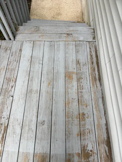 Weathered wood deck with peeling paint leading down stairs to a gravel path.