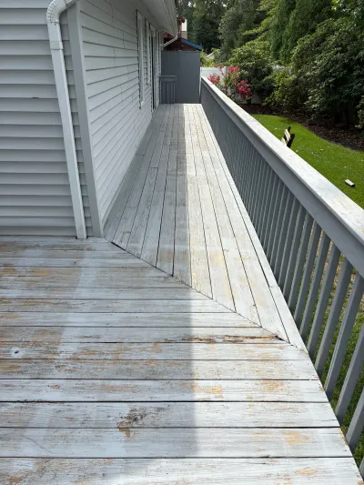 A weathered side deck with peeling paint and worn wood boards runs along the side of a house.