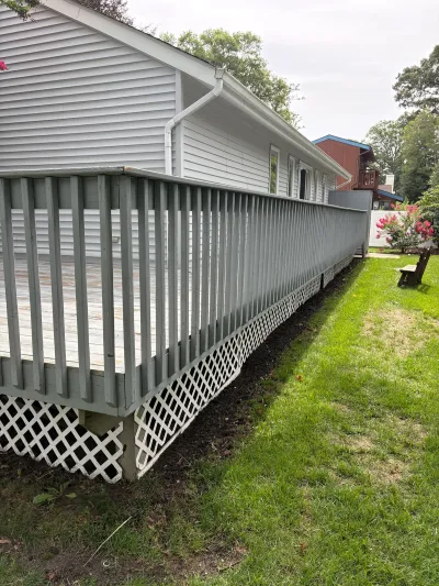 A long wooden deck with grey railings and white lattice skirting runs along the side of a house.