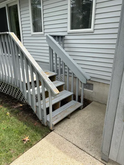 Weathered wooden deck stairs with peeling grey paint leading to two side doors of a house.