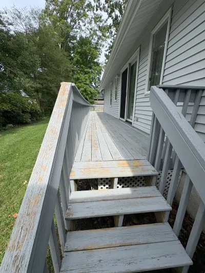 A weathered wood deck and stairway with peeling gray paint along the back of a house.