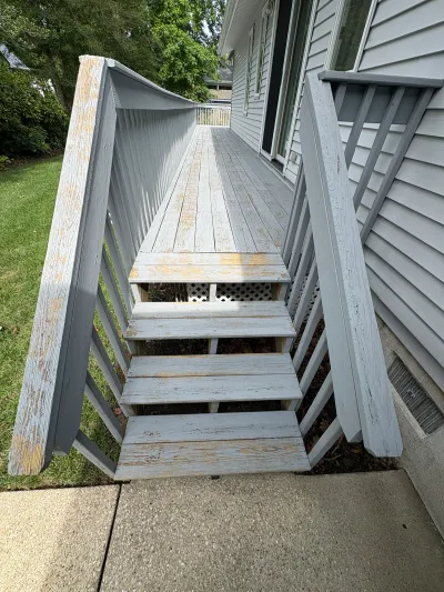 Weathered wooden deck stairs with peeling gray paint leading down to a concrete walkway.