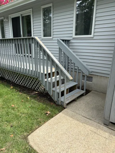 Weathered grey deck and stairway with peeling paint attached to a vinyl-sided house.