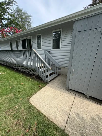 Side exterior of a house with a weathered wood deck, stairs, and an attached shed with cracked siding.