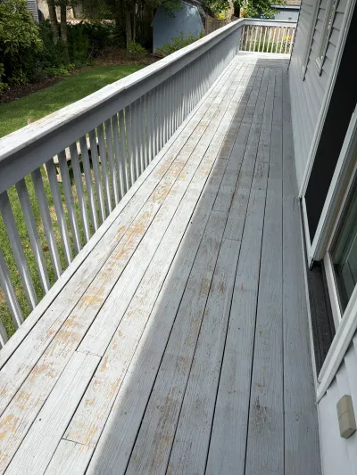 A weathered deck with peeling paint on the boards and railing, running alongside a house.