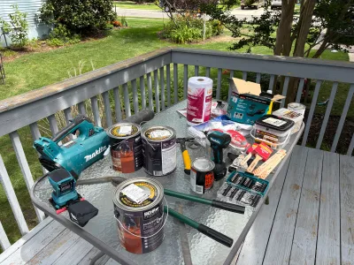 Deck refinishing tools and paint cans staged on an outdoor table before starting work.