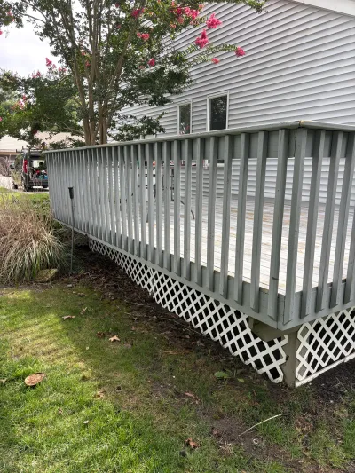 Weathered wood deck with sagging railing and lattice skirting attached to a house with vinyl siding.