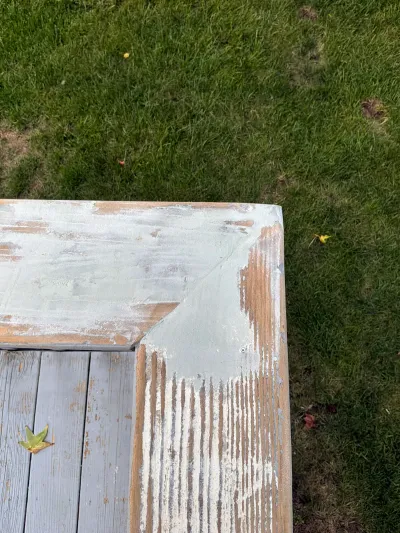 Close-up of weathered wood corner with peeling pale green paint over a grass lawn background.