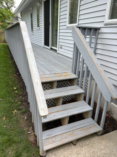 Weathered wood deck stairs and railing with peeling paint alongside a house exterior.