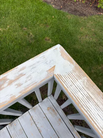 Close-up of a weathered wooden bench corner with peeling paint, sitting on a lawn.