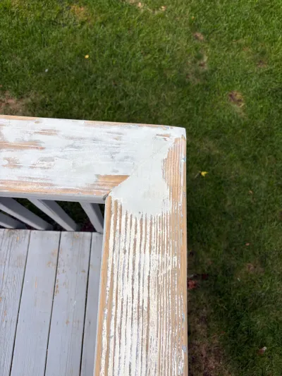 Weathered deck railing post with peeling paint exposing bare wood grain above a lawn.