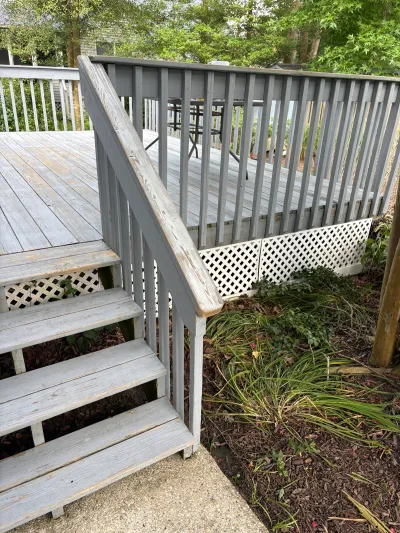 Weathered grey wood deck with peeling paint and a stairway leading down to a concrete landing.