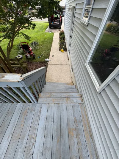Weathered wooden deck stairs beside a house, viewed from above looking toward a side yard.