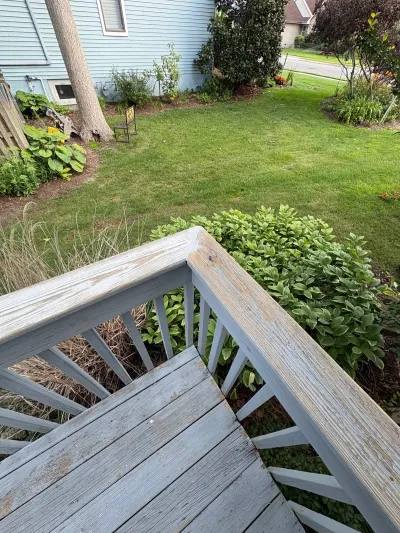 Weathered wooden deck stairs and railing with peeling paint overlooking a backyard lawn and garden beds.