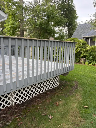 Weathered wood deck with grey painted railing and white lattice skirting in a backyard.