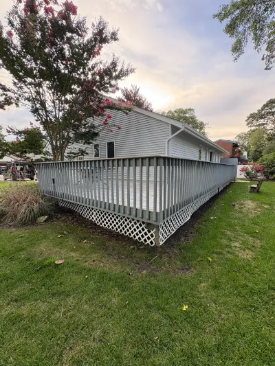 Rear view of a house with light grey vinyl siding and a raised wood deck with lattice skirting.