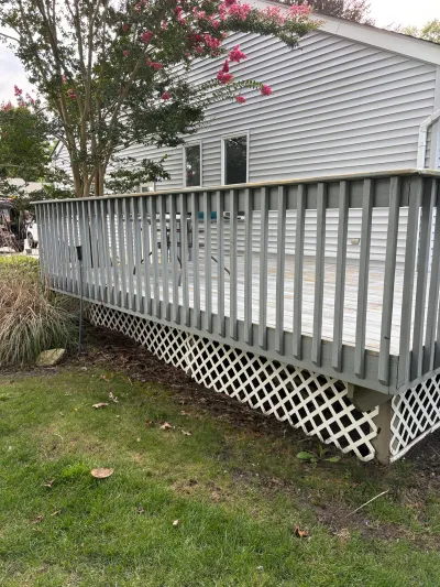 Weathered backyard deck with grey railing and lattice skirting beside a vinyl-sided house.