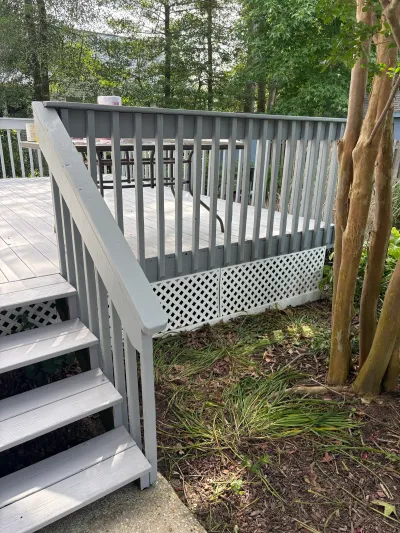 A grey-painted wood deck with staircase and white lattice skirting, surrounded by trees and garden beds.