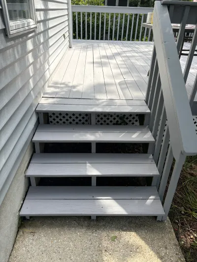 Grey-painted wood deck stairs with lattice skirting leading down to a concrete patio.